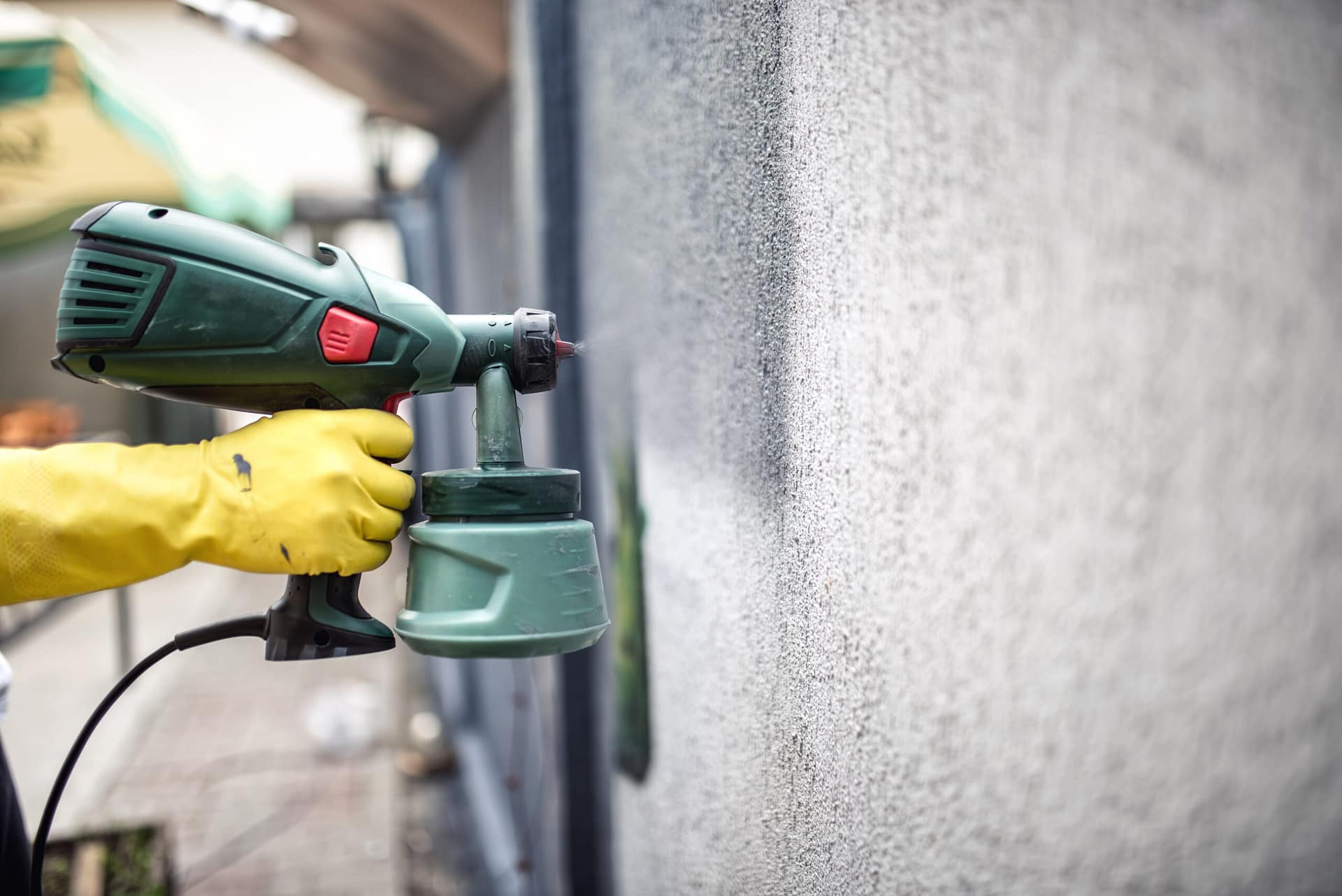 Worker painting wall with grey paint using professional spray gun