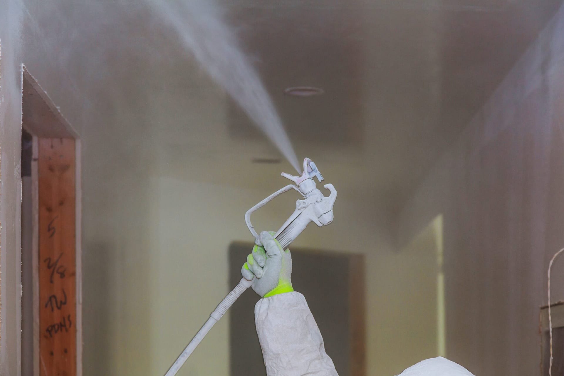 Worker painting wall with spray gun in white color.